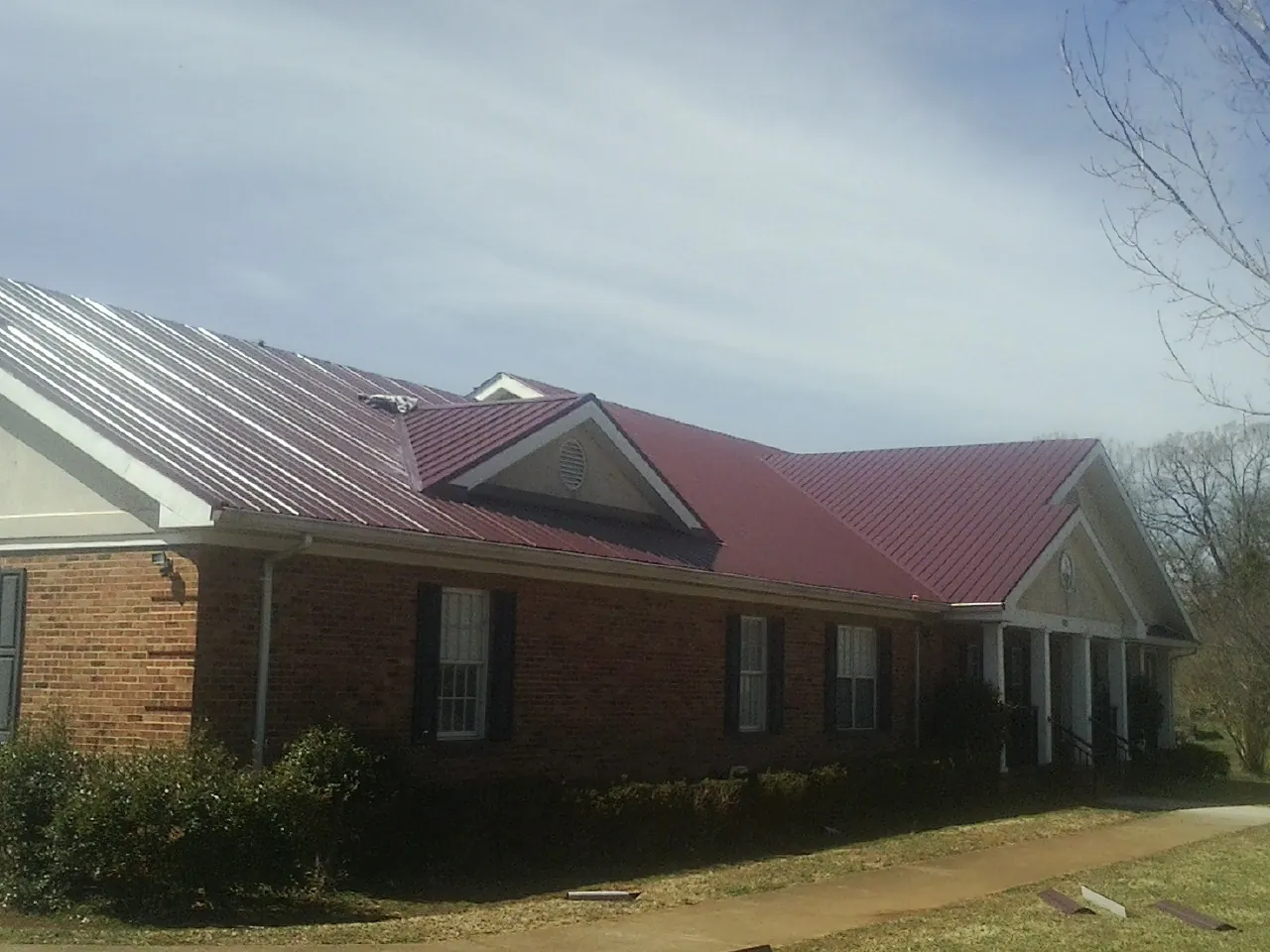 Red metal roof with gabled entries on a long brick building, from a Hail Damage Roof Repair job in Perkiomenville
