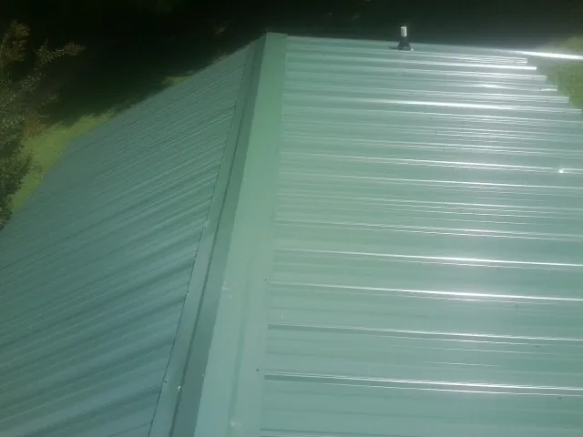 New green metal panels meeting at the ridge of a roof — Flat Roof Repair work by our crew in Perkiomenville