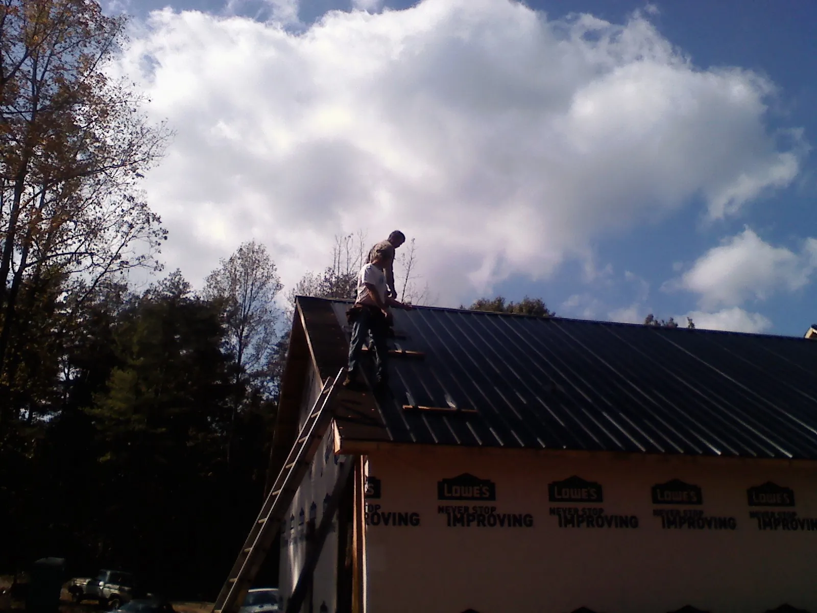 Roofer fastening dark metal panels high against a cloudy sky, from a Roof Inspection job in Perkiomenville
