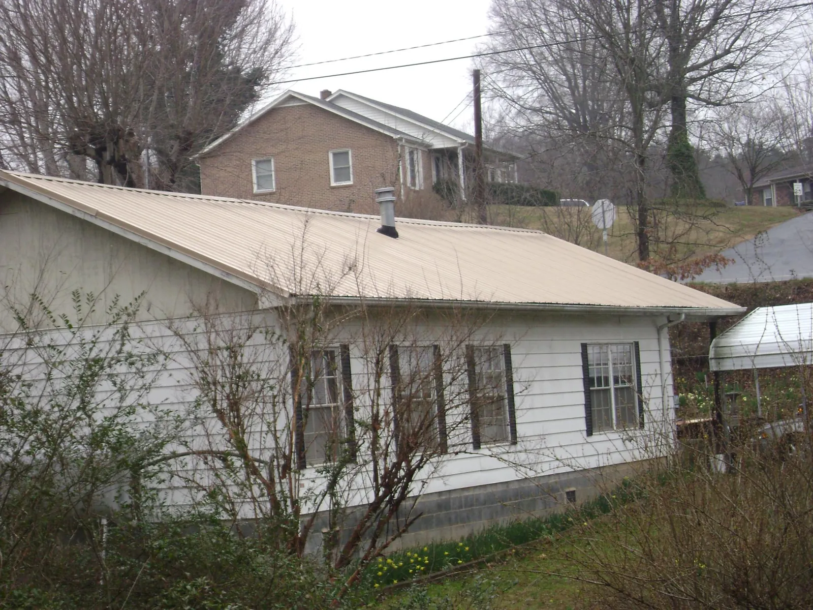 Tan metal roof on a white sided house set into a hillside — Commercial Roofing by Roofing Brothers in Perkiomenville